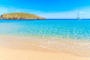 Güzel kumlu Cala Comte plajı ve denizdeki katamaran teknesi, İbiza Adası, İspanya