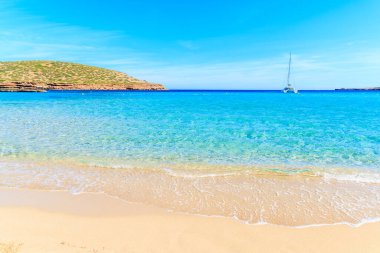Güzel kumlu Cala Comte plajı ve denizdeki katamaran teknesi, İbiza Adası, İspanya