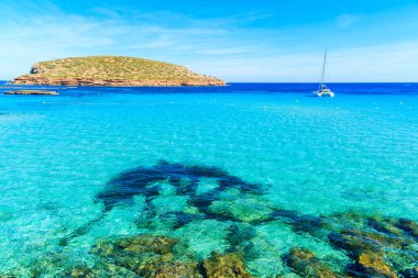 Cala Comte Körfezi 'nin güzel turkuaz suyu ve arka planda katamaran teknesi, İbiza Adası, İspanya