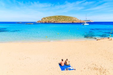Kimliği belirsiz genç bir çift güzel kumlu Cala Comte plajında güneşleniyor mavi deniz suyuyla, İbiza adası, İspanya