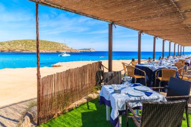 CALA COMTE BAY, IBIZA Adası- 17 Mayıs 2017: İspanya 'nın İbiza adasında misafirlerin muhteşem deniz manzarasının keyfini çıkarabilecekleri Cala Comte sahilindeki lüks sahil restoranının gölgeli terasında masalar.