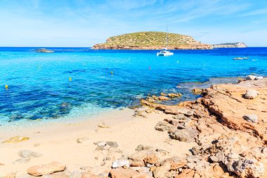Cala Comte Körfezi 'nin güzel turkuaz suyu ve arka planda katamaran teknesi, İbiza Adası, İspanya