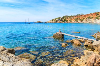 Kimliği belirsiz bir kadın Cala d 'Hort körfezindeki küçük ahşap iskelede oturuyor ve İspanya' nın İbiza adasındaki Es Vedra adasını görüyor.