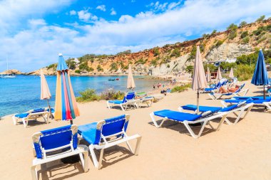 Güneş yatakları, şemsiyeler ve güzel mavi deniz suyuyla Cala d 'Hort plajı manzarası, İbiza Adası, İspanya