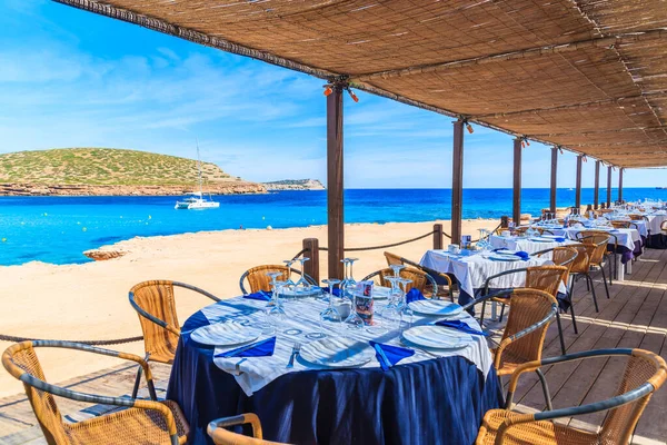CALA COMTE BAY, IBIZA Adası- 17 Mayıs 2017: İspanya 'nın İbiza adasında misafirlerin muhteşem deniz manzarasının keyfini çıkarabilecekleri Cala Comte sahilindeki lüks sahil restoranının gölgeli terasında masalar.