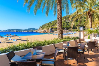 CALA SAN VICENTE BAY, IBIZA ADASI - 19 Mayıs 2017: Cala San Vicente Körfezi, İbiza Adası, İspanya 'da palmiye ağaçları olan plajdaki bar masaları.
