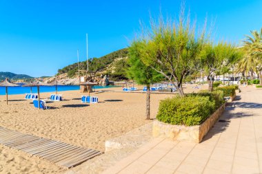 Güneşli yaz gününde Cala San Vicente koyunda şemsiyeli ve güneşli kumsal, İbiza adası, İspanya