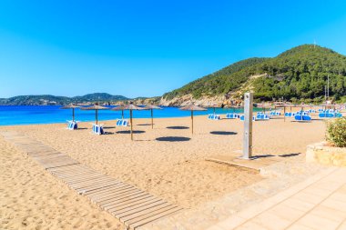 Güneşli yaz gününde Cala San Vicente koyunda şemsiyeli ve güneşli kumsal, İbiza adası, İspanya