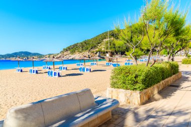 Güneşli yaz gününde Cala San Vicente koyunda şemsiyeli ve güneşli kumsal, İbiza adası, İspanya