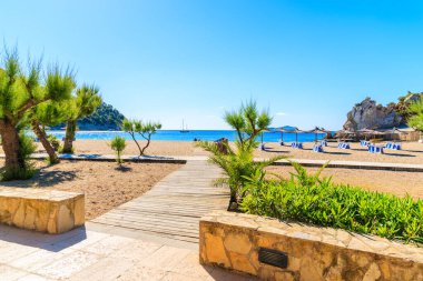 Güneşli yaz gününde İspanya 'nın İbiza adasında Cala San Vicente Körfezi' nde şemsiyeli ve güneşli yataklı kumsala giden yol.