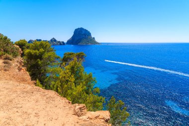 İspanya 'nın İbiza adası Cala d' Hort körfezindeki Es Vedra adası ve mavi denizde motorlu tekne manzarası