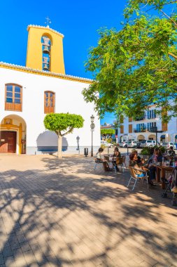 SANTA GERTRUDIS DE FRUTERA, IBIZA ADASI - 19 Mayıs 2017: İspanya 'nın İbiza adasındaki Santa Getrudis kasabasındaki kilise meydanındaki restoranlarda oturan insanlar.