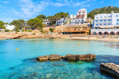 Cala Portinatx Körfezi 'ndeki İbiza adası, mavi deniz suyuyla dolu otel ve restoran binaları.