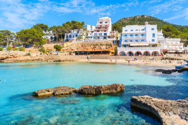 Cala Portinatx Körfezi 'ndeki İbiza adası, mavi deniz suyuyla dolu otel ve restoran binaları.