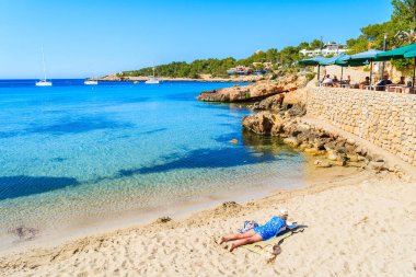 CALA PORTINATX, IBIZA ADASI - 22 Mayıs 2017: İspanya 'nın İbiza adasındaki Cala Portinatx körfezinde yatan ve kitap okuyan kadın.