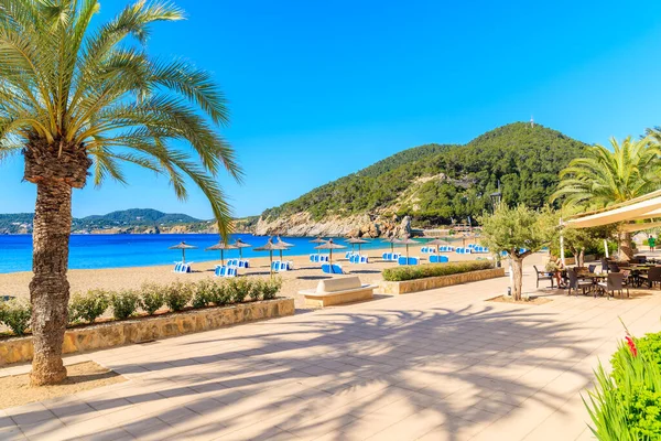 Güneşli yaz gününde Cala San Vicente Körfezi 'nde restoranları ve barları olan kumlu sahil şeridi boyunca gezinti, İbiza Adası, İspanya