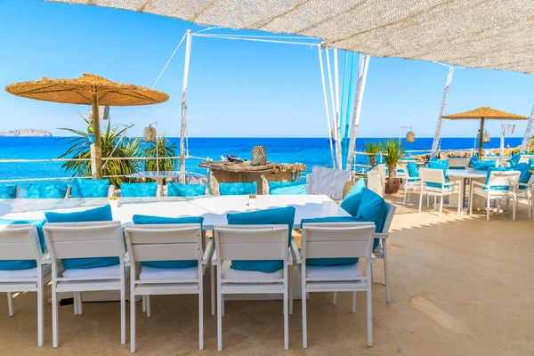 CALA NOVA BEACH, IBIZA ADASI - 20 Mayıs 2017: Cala Nova sahilindeki güzel deniz manzaralı restoran terasında beyaz masa ve mavi yastıklı sandalyeler, İbiza Adası, İspanya.