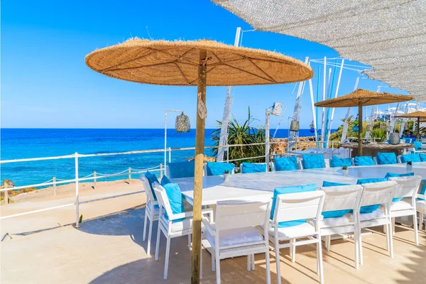 CALA NOVA BEACH, IBIZA ADASI - 20 Mayıs 2017: Cala Nova sahilindeki güzel deniz manzaralı restoran terasında beyaz masa ve mavi yastıklı sandalyeler, İbiza Adası, İspanya.