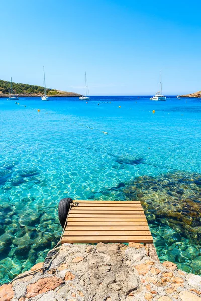 Ahşap iskele ve mavi deniz manzarası. Uzaklarda yelkenli tekneleri var. Cala Portinatx Körfezi, İbiza Adası, İspanya.