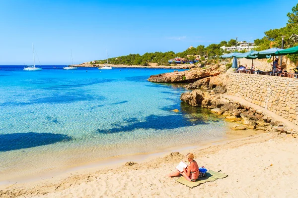CALA PORTINATX, IBIZA ADASI - 22 Mayıs 2017: İspanya 'nın İbiza adasındaki Cala Portinatx körfezinde oturan ve kitap okuyan kadın.