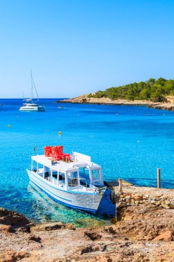 İspanya 'nın İbiza adasındaki Cala Portinatx Körfezi' nde demirleyen turistler için beyaz ve mavi feribot.