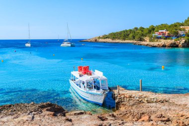 İspanya 'nın İbiza adasındaki Cala Portinatx Körfezi' nde demirleyen turistler için beyaz ve mavi feribot.