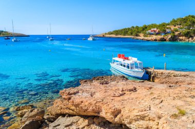 İspanya 'nın İbiza adasındaki Cala Portinatx Körfezi' nde demirleyen turistler için beyaz ve mavi feribot.