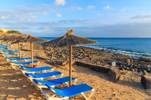 A napozóágyak és a napernyők a Playa Blanca tengerparti naplemente időben sor — Stock Fotó