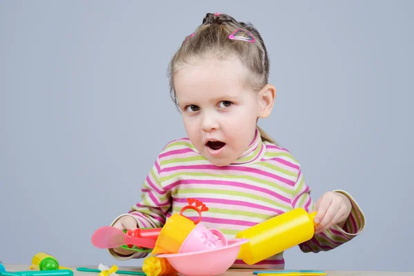 Menina brincando com utensílios de mesa de plástico — Fotografia de Stock