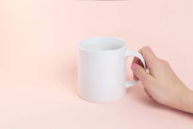 Beyaz kupa modeli. Şeftali renkli arka planda bir kadının el ele tutuşması. Boşluğu kopyala