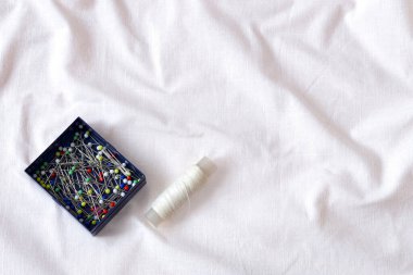 Mavi kutuda iğne dikmek ve buruşmuş beyaz pamuk kumaş üzerinde beyaz iplik makarası. Yumuşak dalgalı kumaş dokusu. Doku örneği modeli