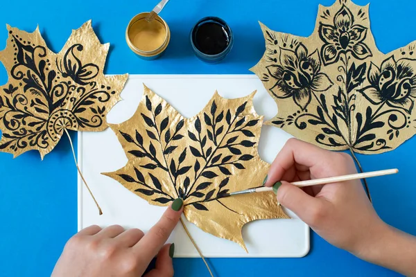 Hand-painted dry autumn maple leaves. Creative art project. Variant 1. Black stylized patterns on gold leaf