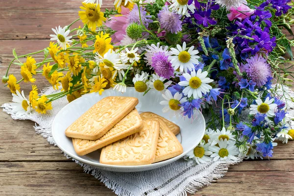 Biscotti in un piattino e un mazzo di fiori selvatici — Foto Stock