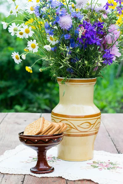 Bolinhos em um vaso cerâmico e um buquê de flores silvestres — Fotografia de Stock