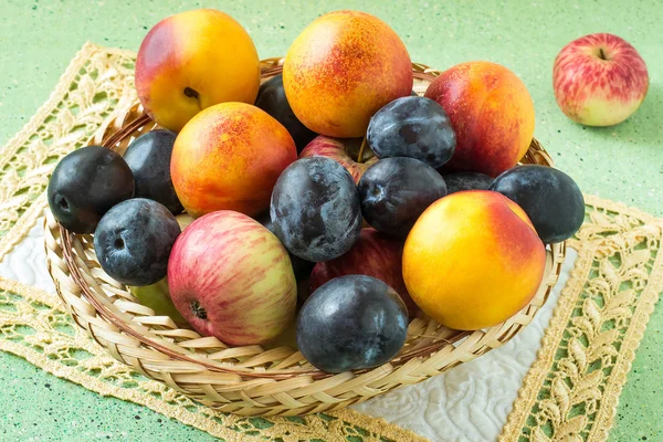 Много слив, яблок и нектаринов в плетеной корзине — стоковое фото