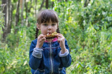 Little girl at the picnic eating with relish chicken leg 