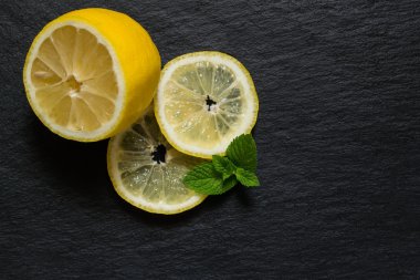 Slices and half a lemon with mint leaves on a slate blackboard