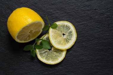 Slices and half a lemon with a sprig of mint on a slate blackboa