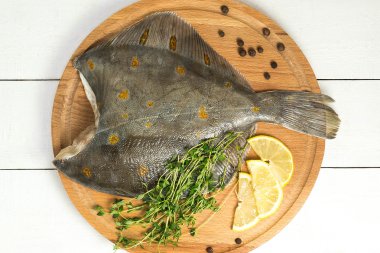 Crude flatfish with lemon, thyme and pepper on the board clipart