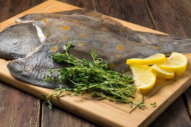 Raw fresh flounder with thyme and lemon on the board clipart