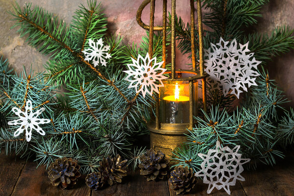 Старая лампа с горящей свечой в ветвях елки

