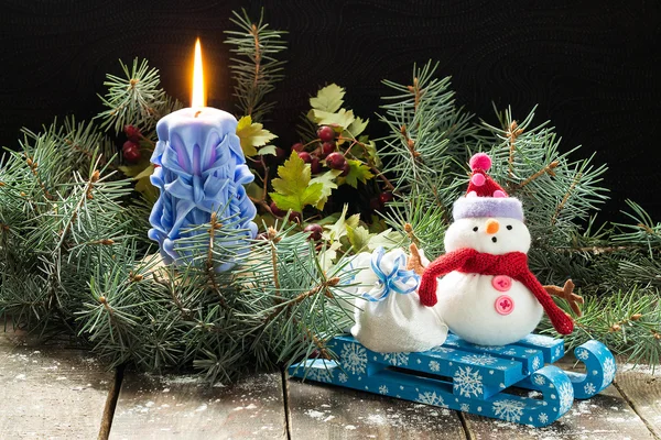 Brennende Kerze in den Fichtenzweigen, Schneemann auf einem Schlitten mit — Stockfoto