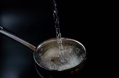 Su siyah bir arka planda tavaya dökülüyor.