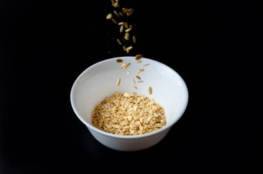 Tahta kaseden uçan yulaf lapaları beyaz ve siyah arka planda izole edilmiş, düşen yulaflar.