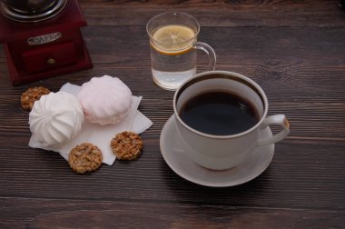 Kahve öğütücüsüyle kahve kompozisyonu, bir fincan kahve, kurabiye ve marşmelov ile koyu bir ağacın arka planında.