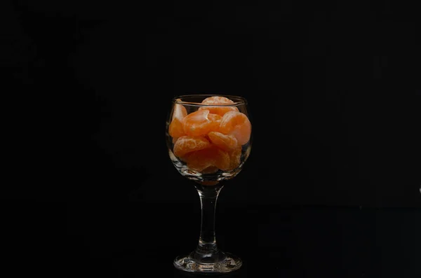 Geschälte Mandarine in einem Glas auf schwarzem Hintergrund — Stockfoto