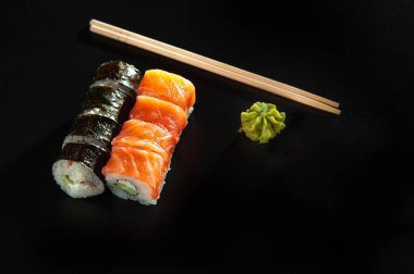 Taze somon, avokado, ananas soslu masago havyarı ve siyah bir masa ve arka plandaki siyah bir tabağa süsleme olarak salata serpiştirilmiş özel suşi rulosu..