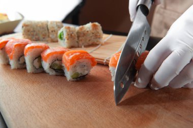 Suşi ustası geleneksel Japon yemeklerini hazırlar. Suşiyi keser.