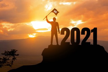 2021 Yeni Yıl Başarı Konsepti. İş adamlarının silueti 2021 ile birlikte dağda bayrak taşıyor..
