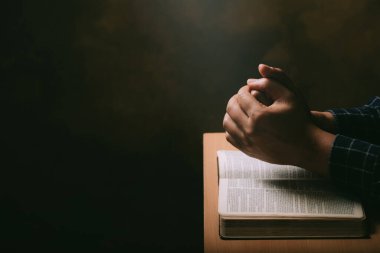 Dua eden genç adam ve İncil 'in elleri ahşap bir masanın arkasında. İnsan dua etmek ve Tanrı' nın, Kutsal İncil 'in, kutsamasını aramak için el ele tutuşur.. 